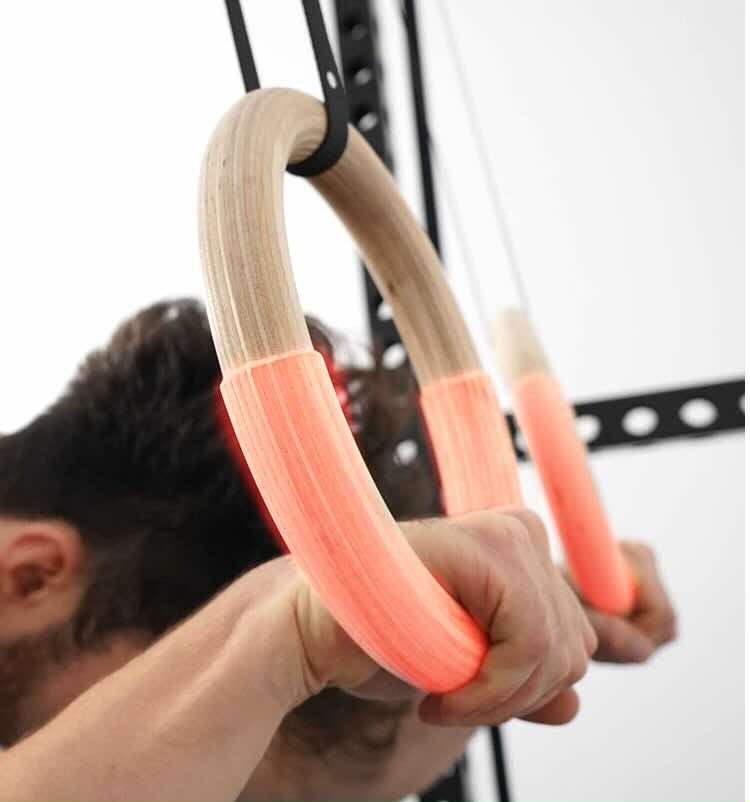 Close-up of a hand gripping the lower arc of a wooden gymnastic ring during a pressing movement, with the gripped section highlighted