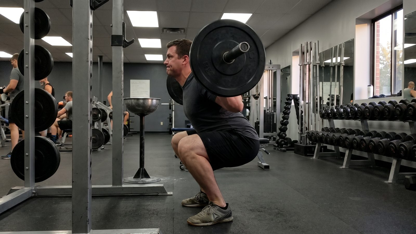 A lifter mid-descent in a barbell back squat inside a power rack, hips travelling back and thighs near parallel