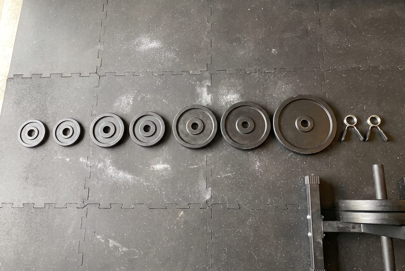 A row of small iron plates laid out on a rubber gym floor from smallest to largest, with a pair of spring collars