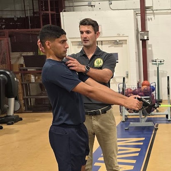 A trainer steadies an athlete's head and shoulder with his hands during a partner neck drill