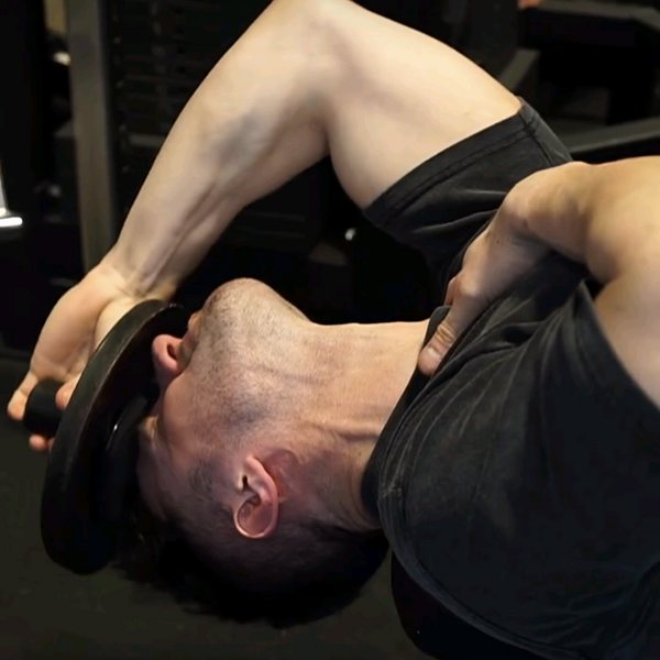 A man lying back off a bench curling his neck with a weight plate held against his forehead