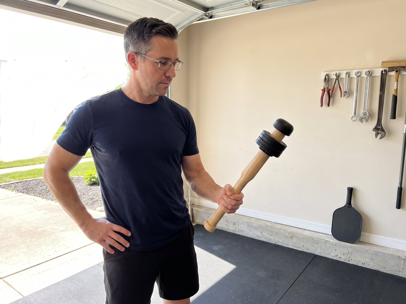 The author in the garage on a sunny morning holding his own wooden club upright in his right hand, the garage door open behind him