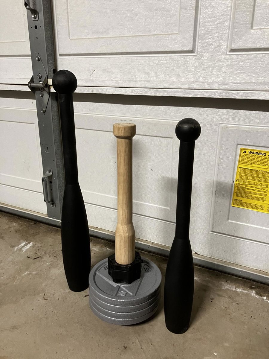 An owner's wooden EZ-CLUB PRO standing on its plate between two black fixed steel clubs in a garage